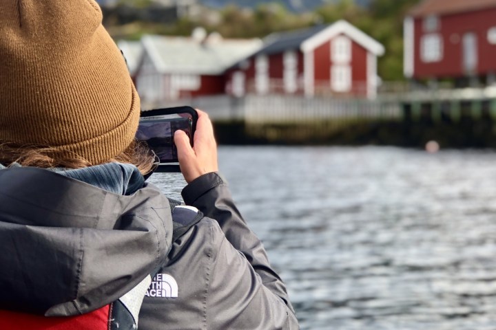 Person kayaking on a lake, photographing red houses with mountains in the background.