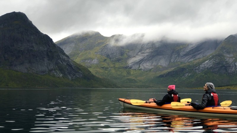 Two people in a kayak on a calm lake with misty mountains in the background.