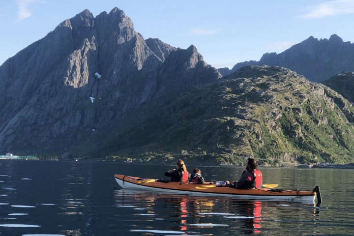 Three people kayaking on a calm lake with large rocky mountains in the background.