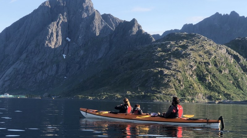 Three people kayaking on a calm lake with large rocky mountains in the background.