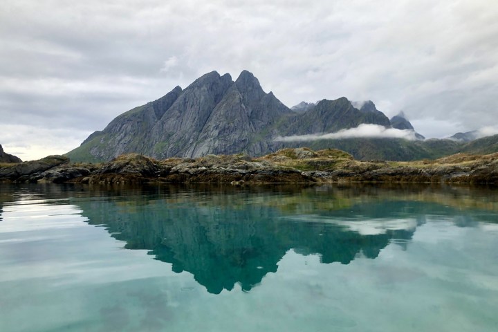 Mountains reflected in clear water beneath a cloudy sky.