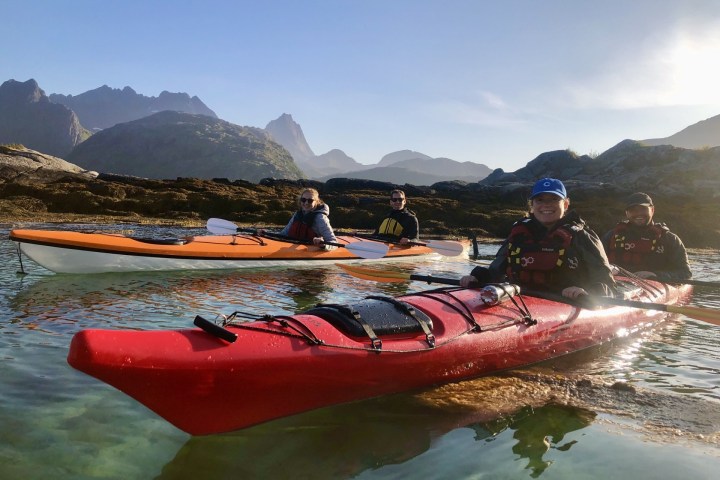 Three people kayaking in clear water with mountains in the background.