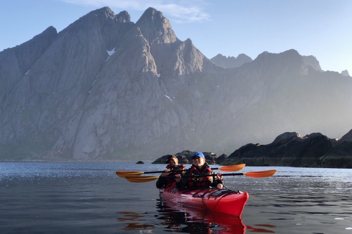 Two people kayaking in a red kayak on calm water with large mountains in the background.