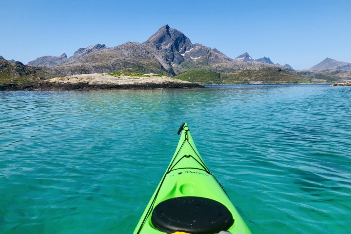 Green kayak on turquoise water with mountains under clear blue sky.
