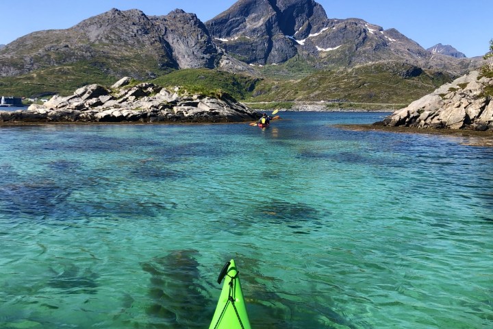 Green kayak on clear blue water with mountains under a blue sky in the background.