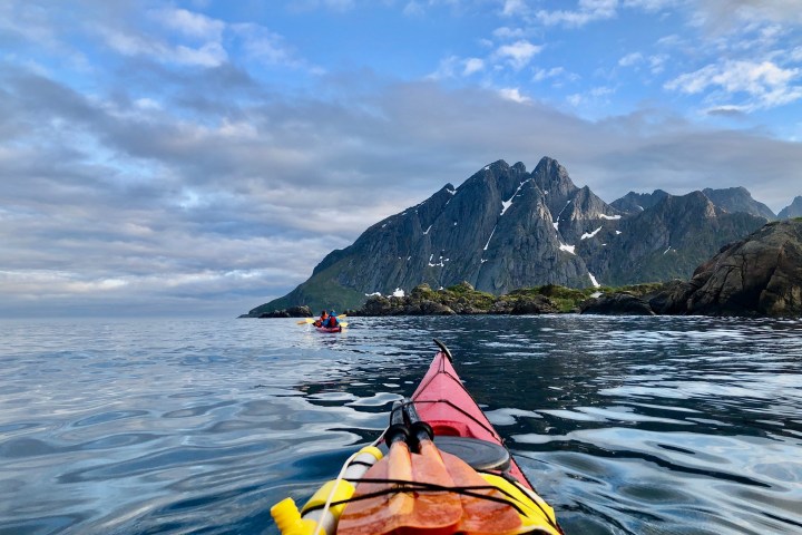 Kayaking on calm sea, mountain view, cloudy sky, with red kayak and paddles in foreground.