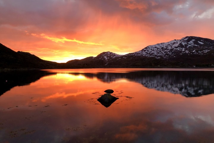 Lake at sunset with vibrant orange sky and reflections of mountains in water.