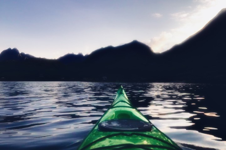 Green kayak on water under a twilight sky with silhouetted mountains.