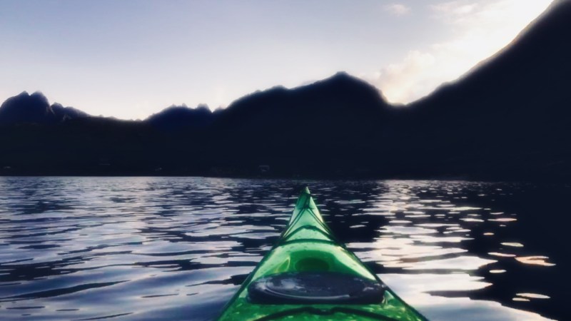 Green kayak on water under a twilight sky with silhouetted mountains.