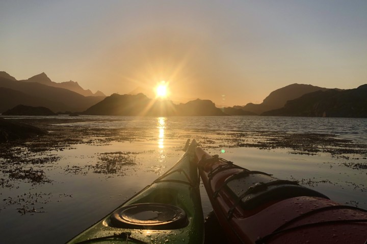Two kayaks on a calm lake at sunset with mountains in the background.