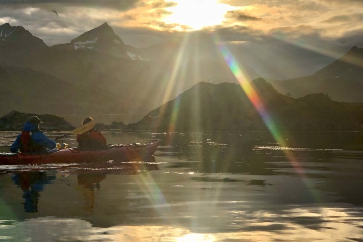 Two people kayaking on calm water at sunset, mountains in the background.