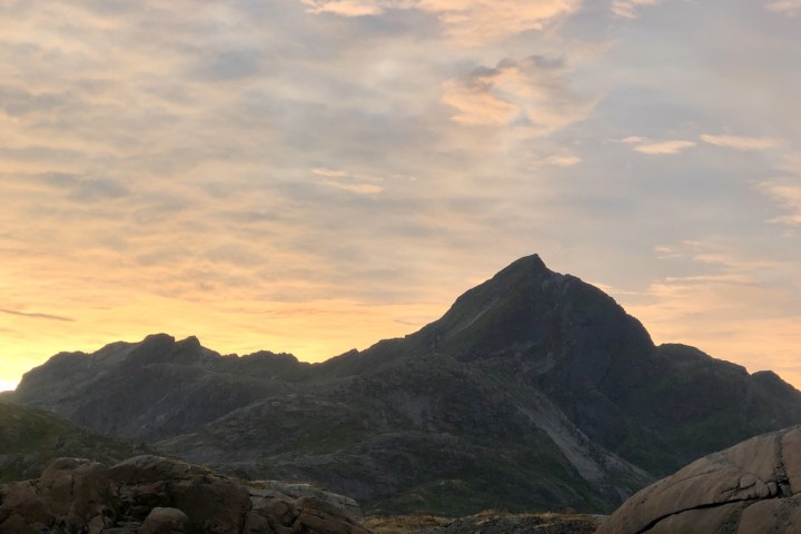 Two people kayaking near rocky shore with mountains and sunset in the background.