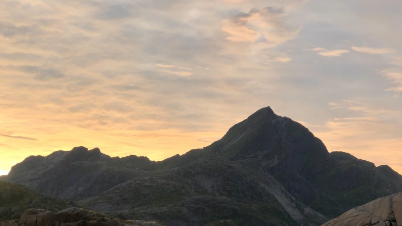 Two people kayaking near rocky shore with mountains and sunset in the background.