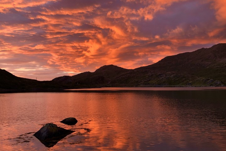 Dramatic orange sunset over a tranquil lake and silhouetted hills.