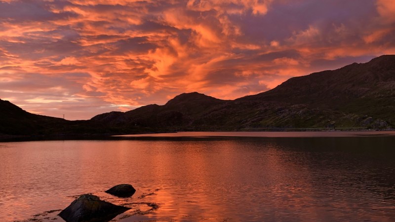 Dramatic orange sunset over a tranquil lake and silhouetted hills.