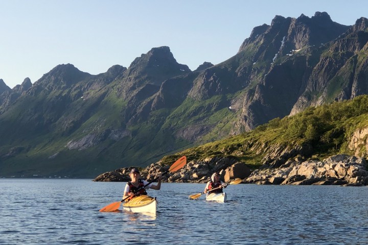 Two people kayaking on a calm lake with mountains in the background.