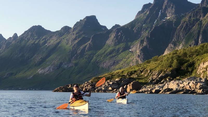Two people kayaking on a calm lake with mountains in the background.