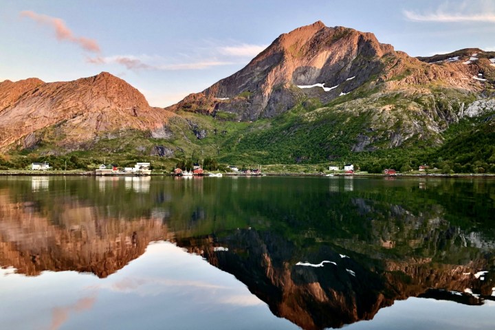 Mountain landscape reflected in a calm lake, with scattered houses along the shoreline.