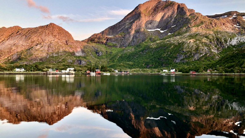 Mountain landscape reflected in a calm lake, with scattered houses along the shoreline.