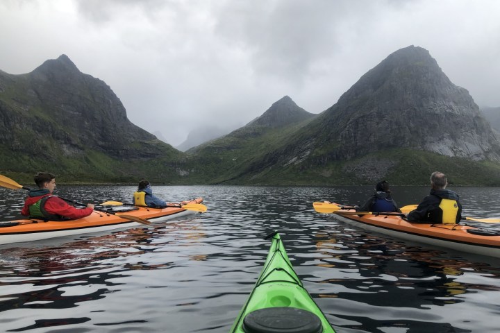 People kayaking on a lake surrounded by mountains under a cloudy sky.