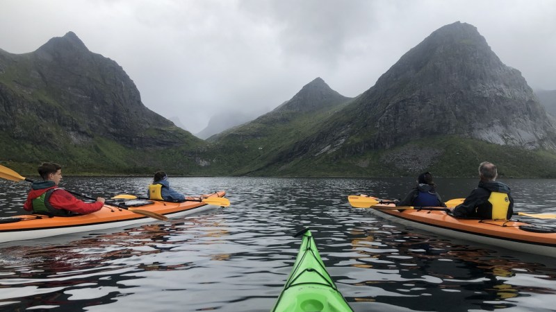 People kayaking on a lake surrounded by mountains under a cloudy sky.