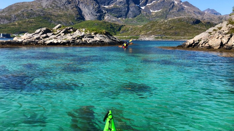 Green kayak on clear turquoise water with mountains in the background.