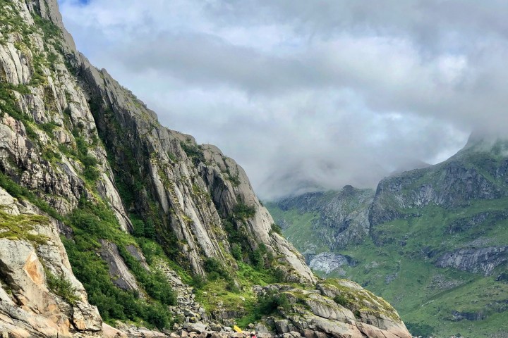 Person kayaking on a calm lake surrounded by steep, green mountains under a cloudy sky.