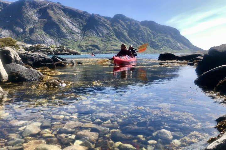 Two people kayaking in a red kayak on clear water with mountains in the background.
