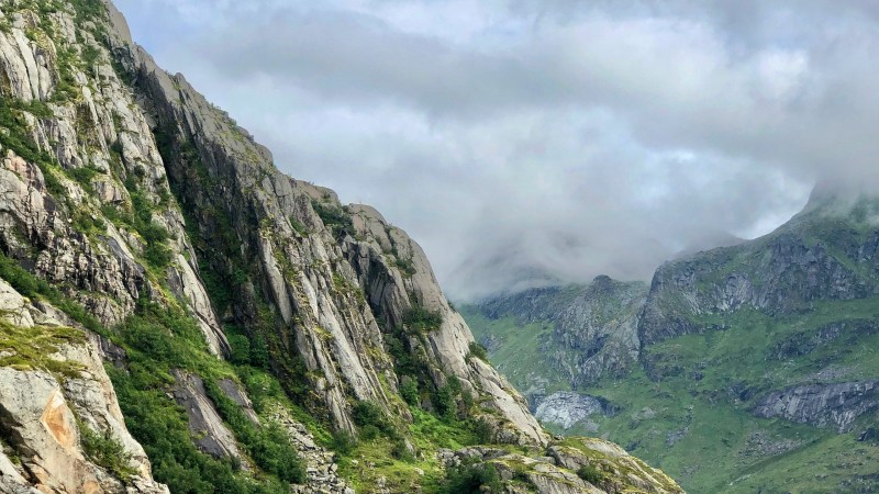 Person kayaking on a lake with steep green cliffs and cloudy sky.