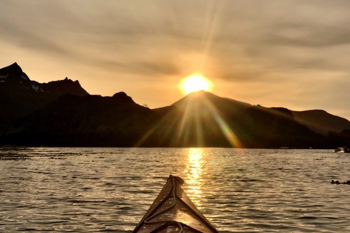 Sunset view from kayak, with sun shining over mountain and reflected on the water.