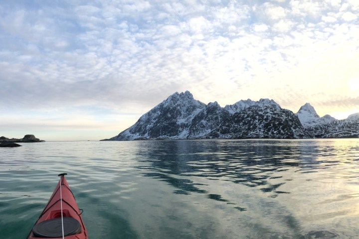 Red kayak on calm sea with snow-covered mountains under cloudy sky.