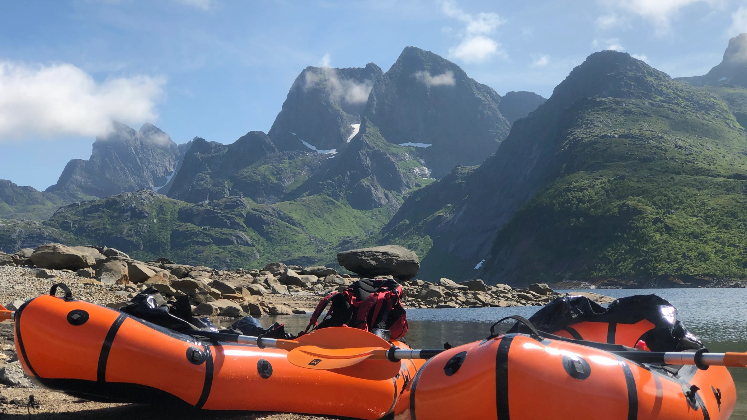 Two orange inflatable kayaks on a rocky shore with mountains in the background.