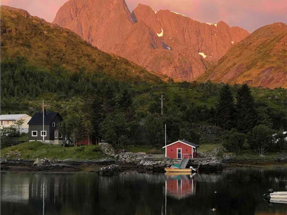 Mountain backdrop at sunset with red cabin and calm lake reflection.