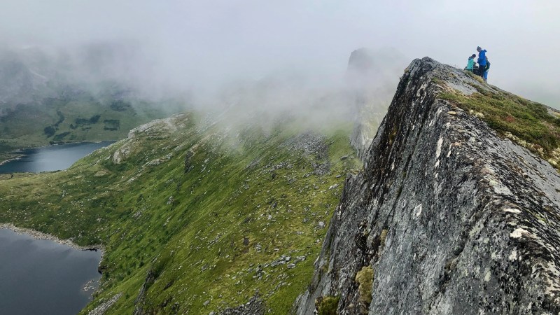 Hikers standing on a misty mountain ridge overlooking a lake and lush valley.