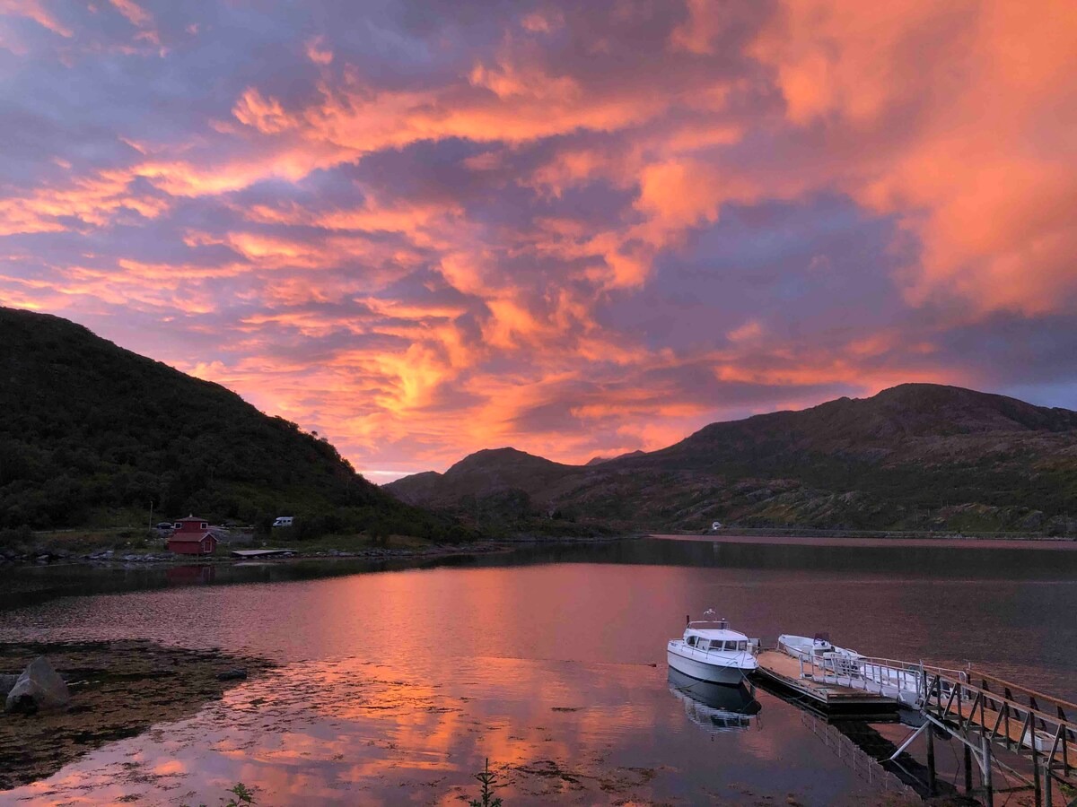Sunset over a tranquil lake with a boat docked and dramatic pink and orange clouds.