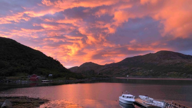 Sunset over a tranquil lake with a boat docked and dramatic pink and orange clouds.