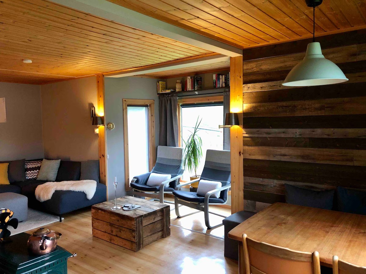 Cozy living room with wooden ceiling, grey sofa, two chairs, wooden coffee table, and pendant lamp.