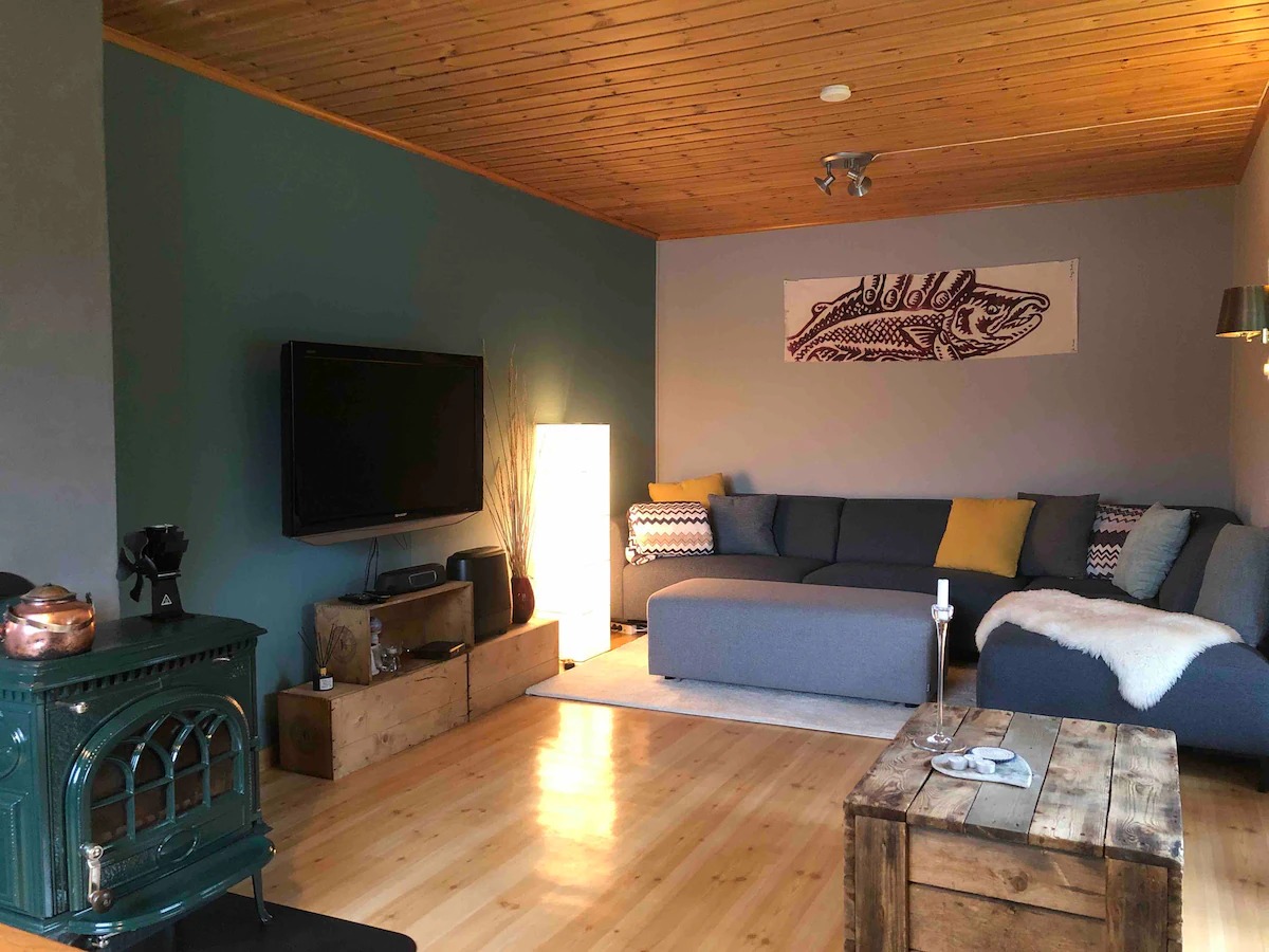 Cozy living room with L-shaped sofa, wood stove, TV, and wooden coffee table.
